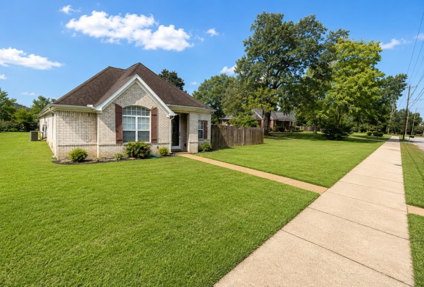 Brick facade residence featuring a front entry, arched window with decorative shutters, established lawn, and concrete sidewalk