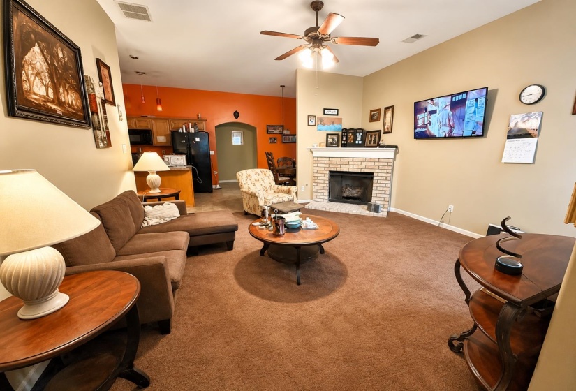 Living area featuring a brick fireplace with a white mantel, ceiling fan, and carpet flooring