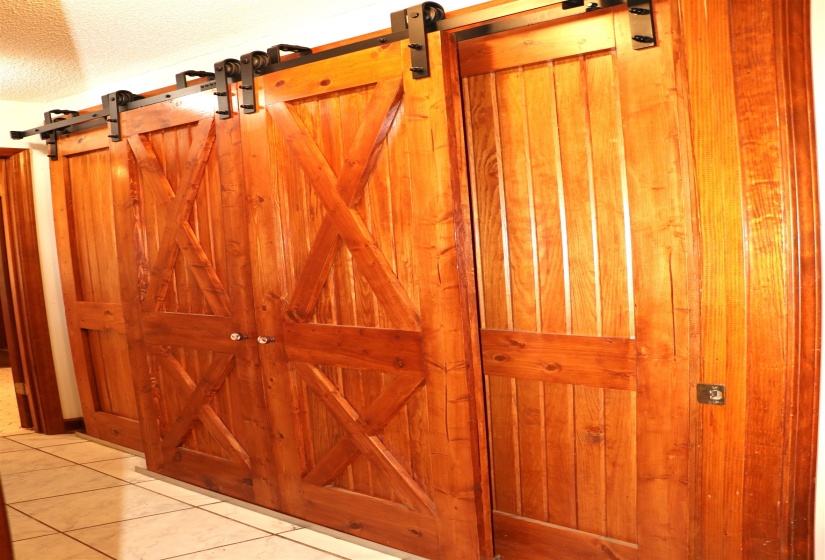 Rustic wood-finish barn doors with black metal hardware, featuring a double door entry with glass knobs and a single plank door with a keyhole