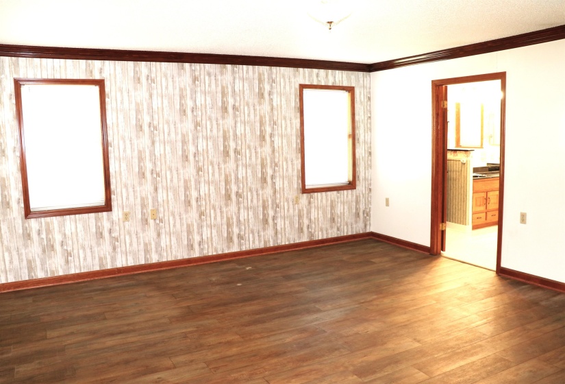 Interior room featuring wood-finish flooring, two windows with wood trim, and a patterned accent wall