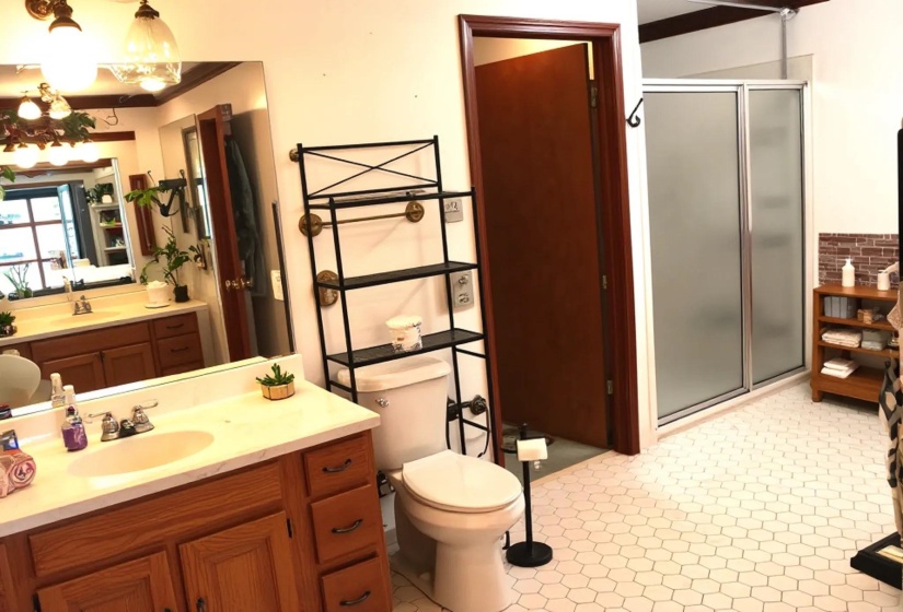 Bathroom featuring hexagonal tile flooring, a dual vanity with oak-finish cabinetry, a shower with frosted glass doors, and a decorative brick-style wall accent