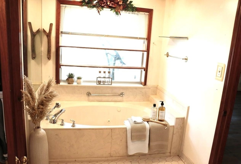 Soaking tub with a tiled surround, chrome fixtures, and a large window with blinds