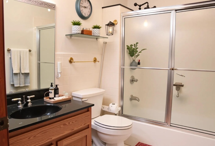 Bathroom featuring a wood-finish vanity with a black countertop and integrated sink, a large mirror, a shower-tub combination with sliding doors, and white tile walls