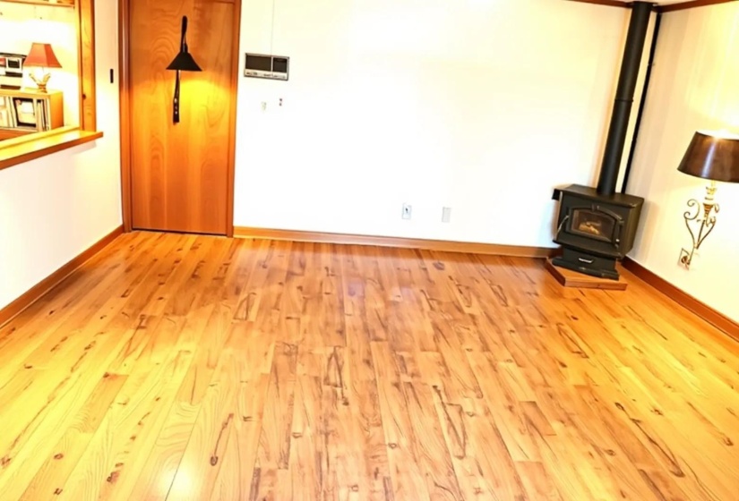 Wood-finish flooring throughout, featuring a corner-installed wood-burning stove with a black stovepipe, a natural wood interior door, and white wall finishes