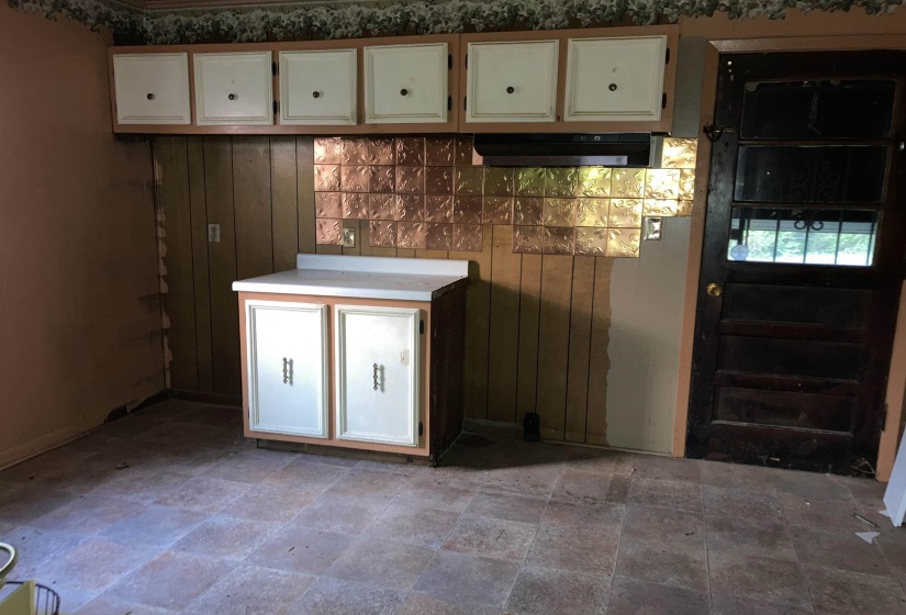 Kitchen featuring light countertops, wood walls, white cabinetry, and stone finish floors