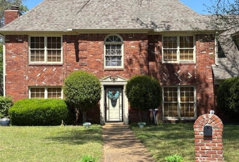 View of front of home featuring a front lawn, brick siding, a chimney, and roof with shingles