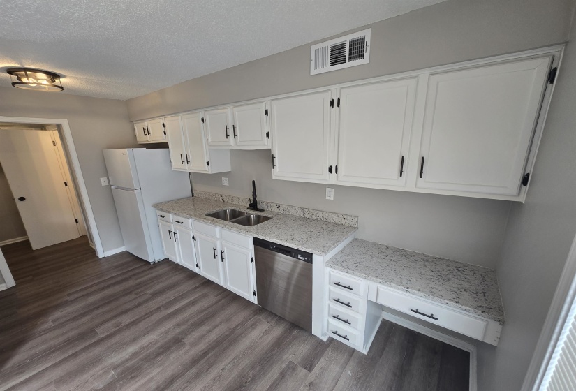 Kitchen with white cabinetry, stainless steel dishwasher, light stone countertops, freestanding refrigerator, and a textured ceiling