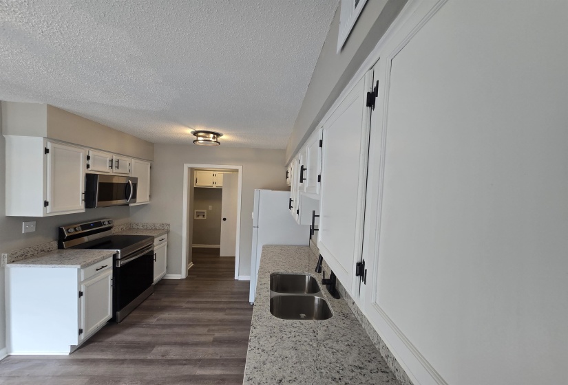 Kitchen with stainless steel appliances, white cabinetry, dark wood-style flooring, light stone counters, and a textured ceiling