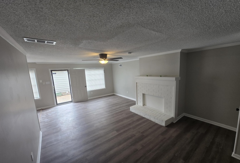 Unfurnished living room with crown molding, a textured ceiling, ceiling fan, dark wood finished floors, and a brick fireplace