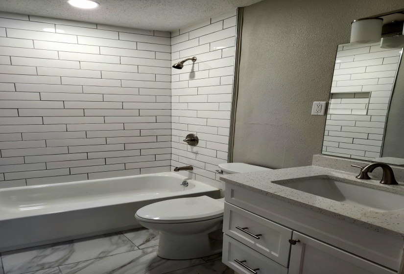 Full bath featuring a textured wall, vanity,  shower combination, light marble finish flooring, and a textured ceiling