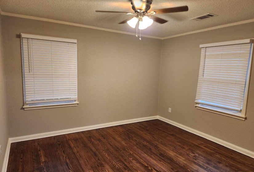 Empty room featuring a textured ceiling, dark wood-type flooring, ornamental molding, ceiling fan, and a textured wall