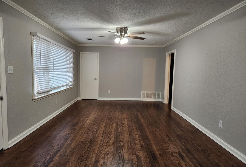 Empty room featuring dark wood-type flooring, a textured ceiling, ornamental molding, a ceiling fan, and a textured wall