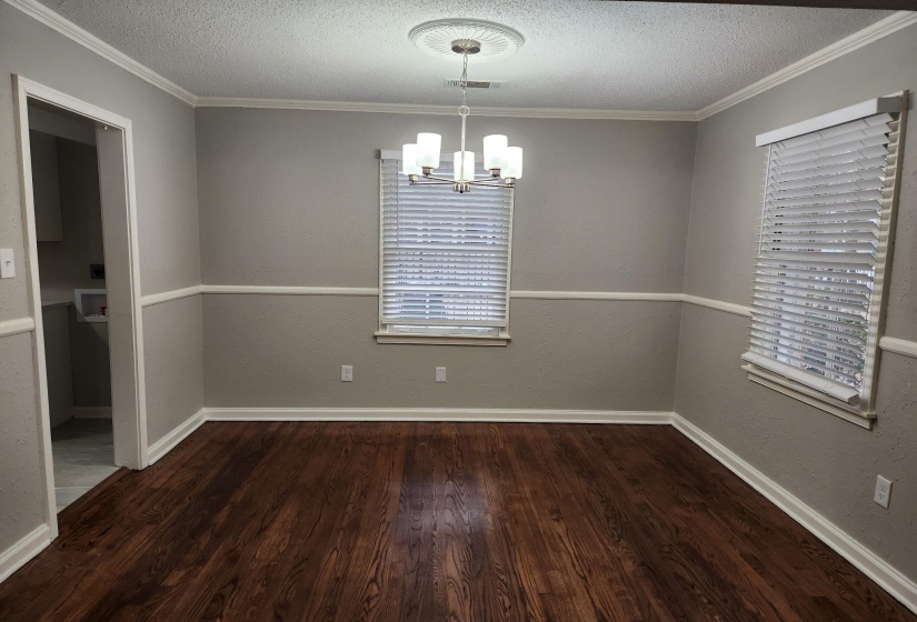 Unfurnished dining area featuring a textured ceiling, a chandelier, ornamental molding, dark wood-style flooring, and a textured wall