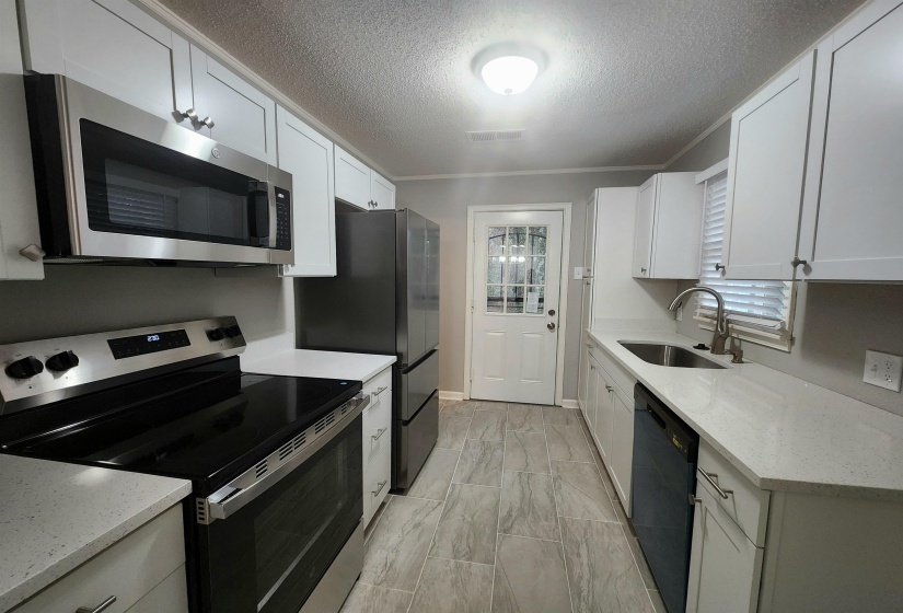 Kitchen featuring appliances with stainless steel finishes, light stone counters, a textured ceiling, white cabinets, and ornamental molding