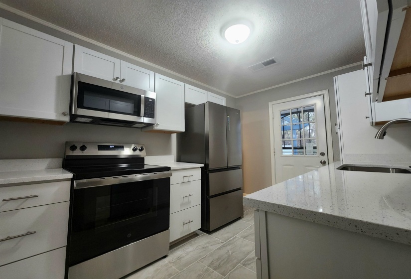 Kitchen featuring appliances with stainless steel finishes, light stone countertops, a textured ceiling, white cabinetry, and crown molding