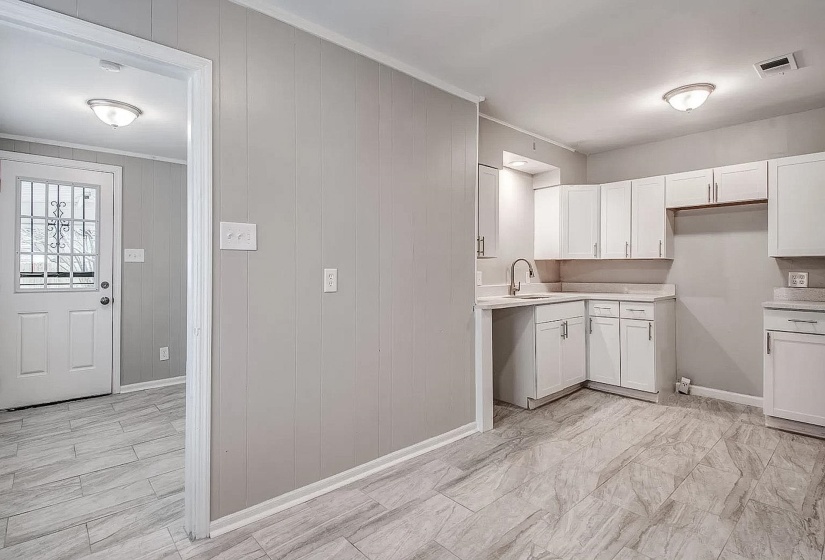Kitchen featuring light countertops, white cabinets, ornamental molding, and wood walls