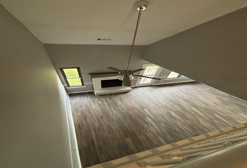 Unfurnished living room with a brick fireplace, a ceiling fan, lofted ceiling, and dark wood finished floors