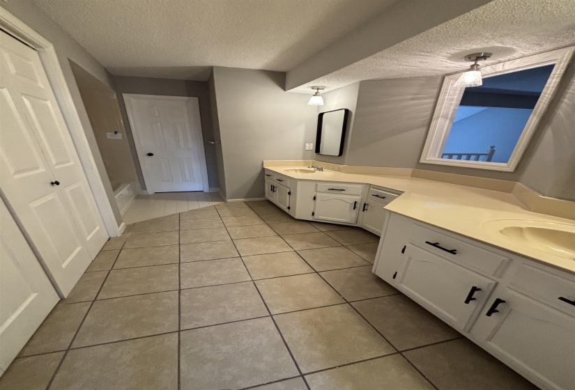 Full bathroom featuring double vanity, a textured ceiling, light tile patterned flooring, and a bath