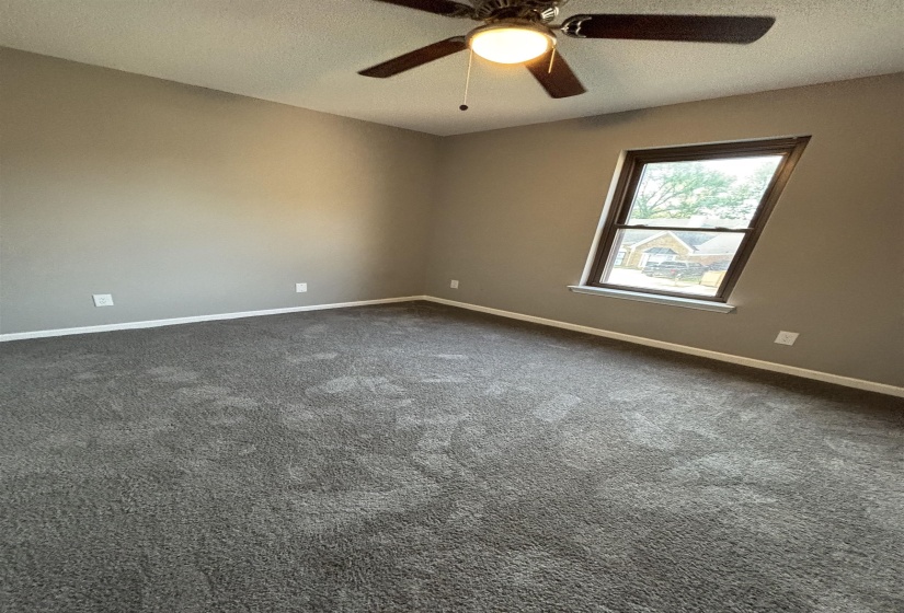 Empty room with a textured ceiling, ceiling fan, and dark colored carpet