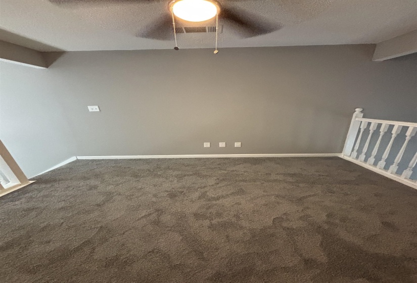 Unfurnished room featuring a textured ceiling, dark carpet, and a ceiling fan