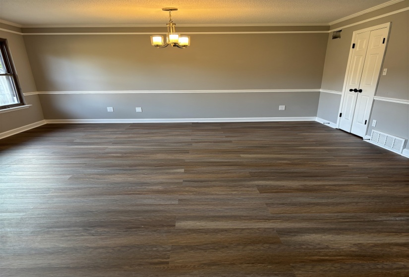 Empty room featuring dark wood-style floors, suspended lighting, ornamental molding, and a textured ceiling