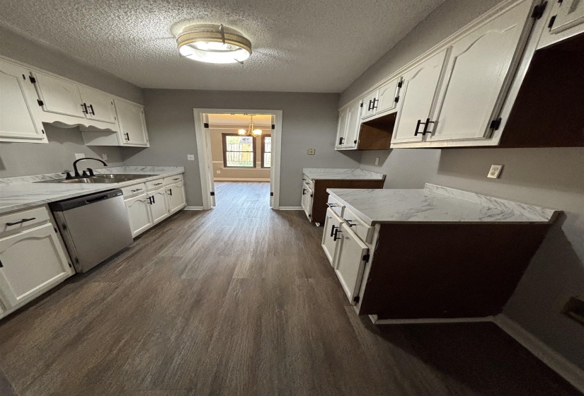 Kitchen with white cabinets, stainless steel dishwasher, dark wood finished floors, a textured ceiling, and hanging lights