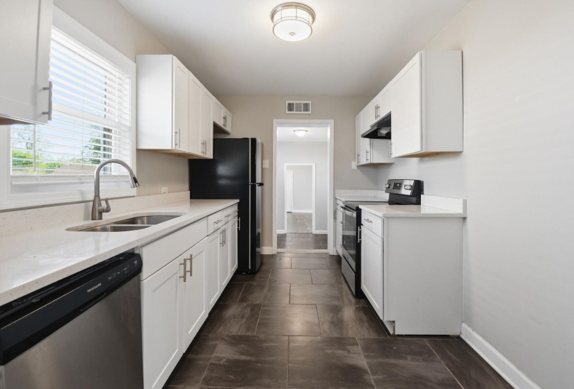 Kitchen with stainless steel appliances, white cabinets, and light stone countertops