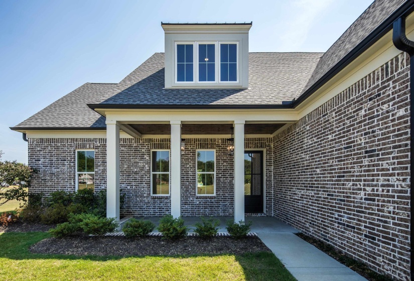 Property entrance with a porch, roof with shingles, brick siding, and a lawn