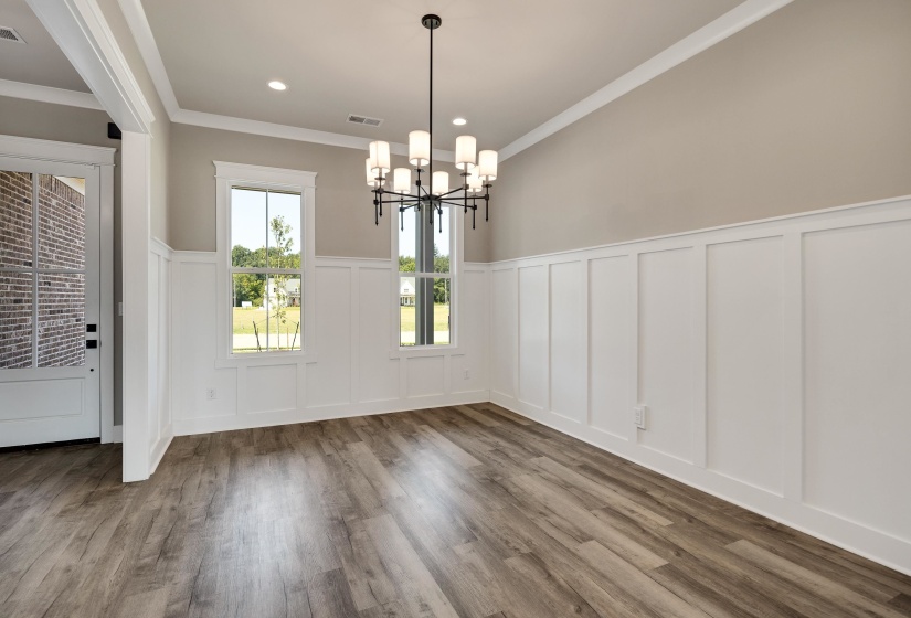 Unfurnished dining area featuring a wainscoted wall, a decorative wall, crown molding, dark wood-style flooring, and hanging lights