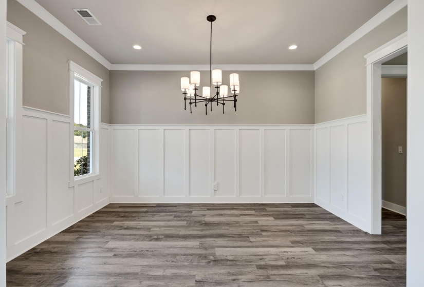 Unfurnished dining area featuring a decorative wall, wainscoting, crown molding, suspended lighting, and dark wood finished floors