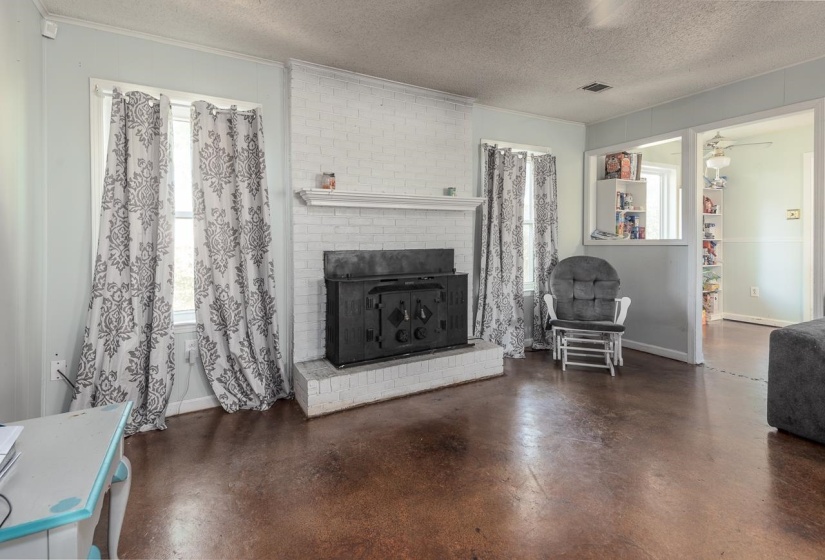 Living room featuring a textured ceiling, crown molding, finished concrete floors, and a brick fireplace