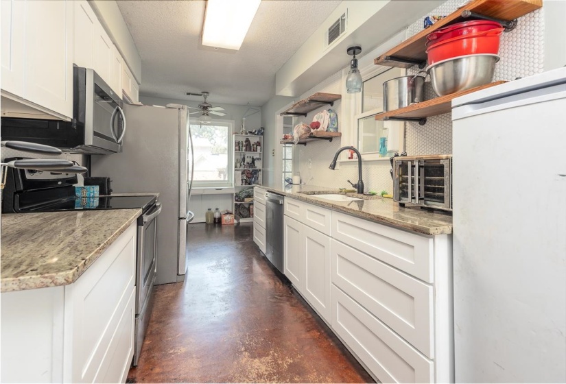 Kitchen with white cabinets, stainless steel appliances, finished concrete floors, light stone counters, and open shelves