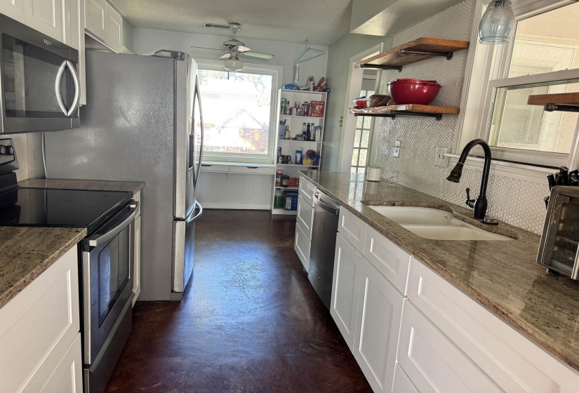 Kitchen with stainless steel appliances, white cabinets, dark stone countertops, concrete flooring, and ceiling fan