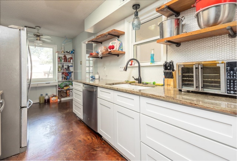 Kitchen featuring tasteful backsplash, white cabinetry, finished concrete flooring, light stone countertops, and stainless steel appliances