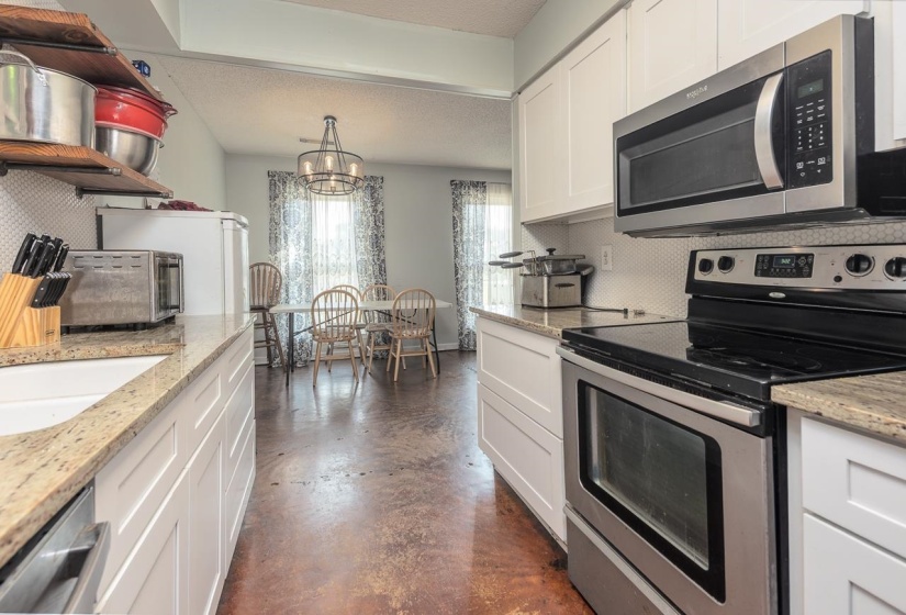 Kitchen with stainless steel appliances, finished concrete flooring, decorative backsplash, white cabinetry, and open shelves