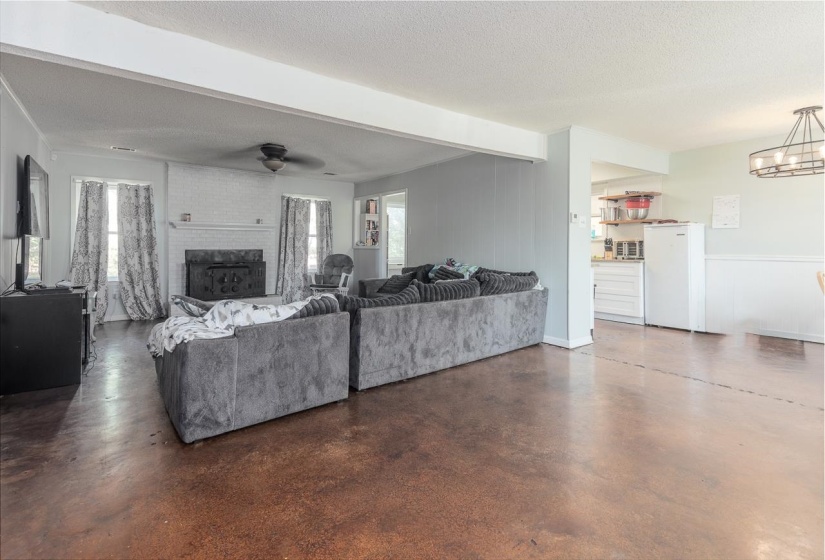 Living room with a fireplace, beam ceiling, a textured ceiling, finished concrete floors, and a ceiling fan