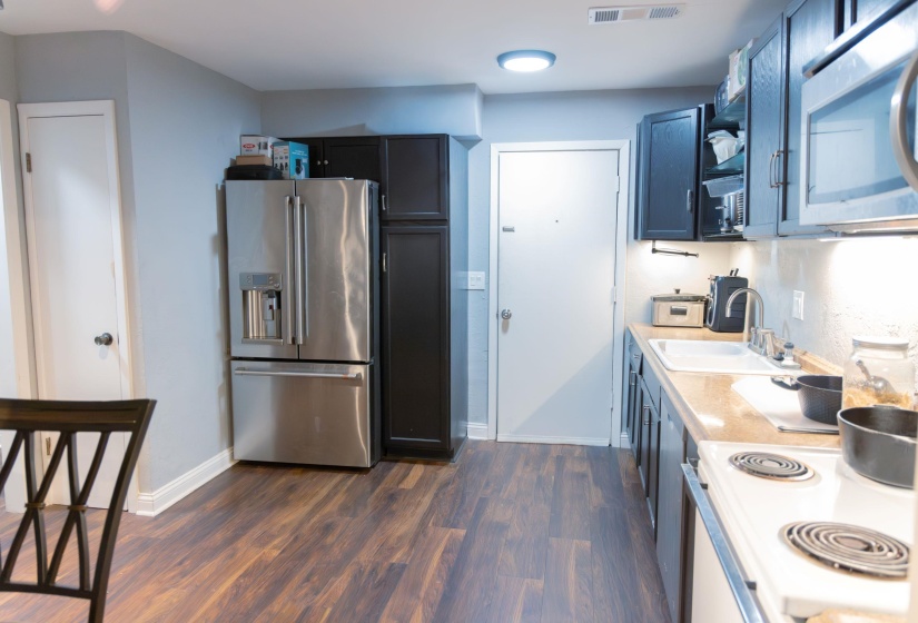 Kitchen featuring stainless steel appliances, light countertops, open shelves, and dark wood finished floors