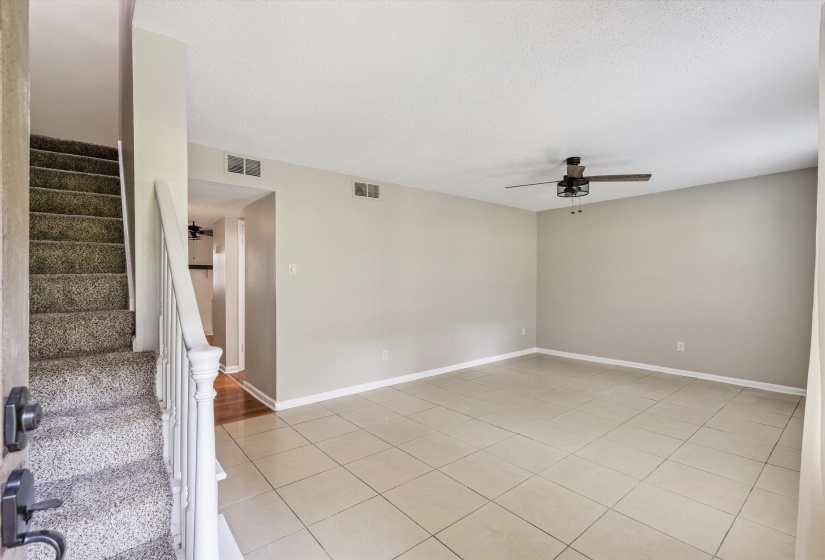 Empty room featuring ceiling fan, stairway, light tile patterned flooring, and a textured ceiling