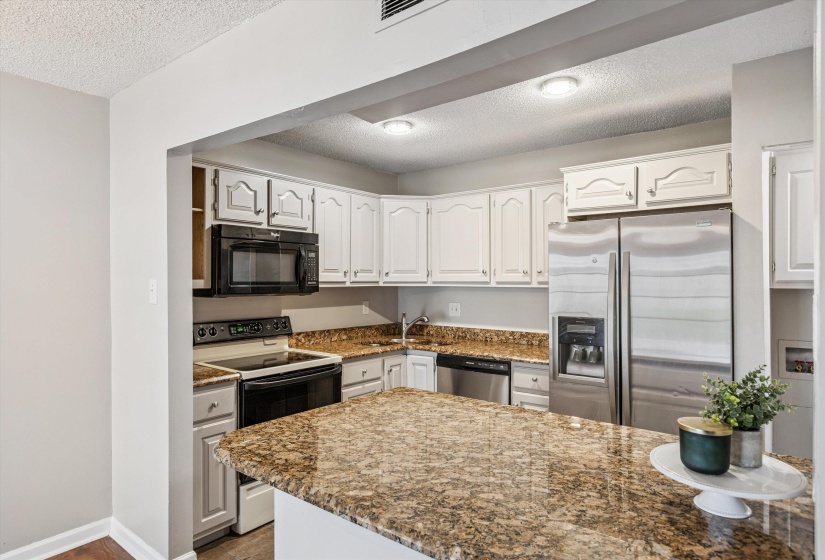 Kitchen with a textured ceiling, appliances with stainless steel finishes, white cabinetry, dark stone countertops, and wood finished floors
