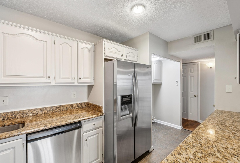 Kitchen featuring appliances with stainless steel finishes, a textured ceiling, white cabinetry, light stone countertops, and dark tile patterned floors