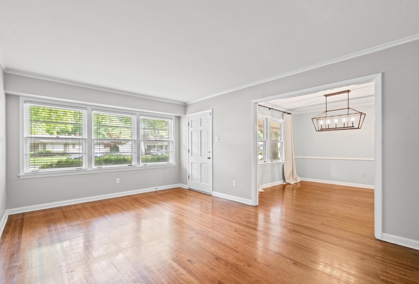 Hardwood flooring throughout, multiple windows, a white paneled entry door, and a framed opening to a separate room with a geometric chandelier