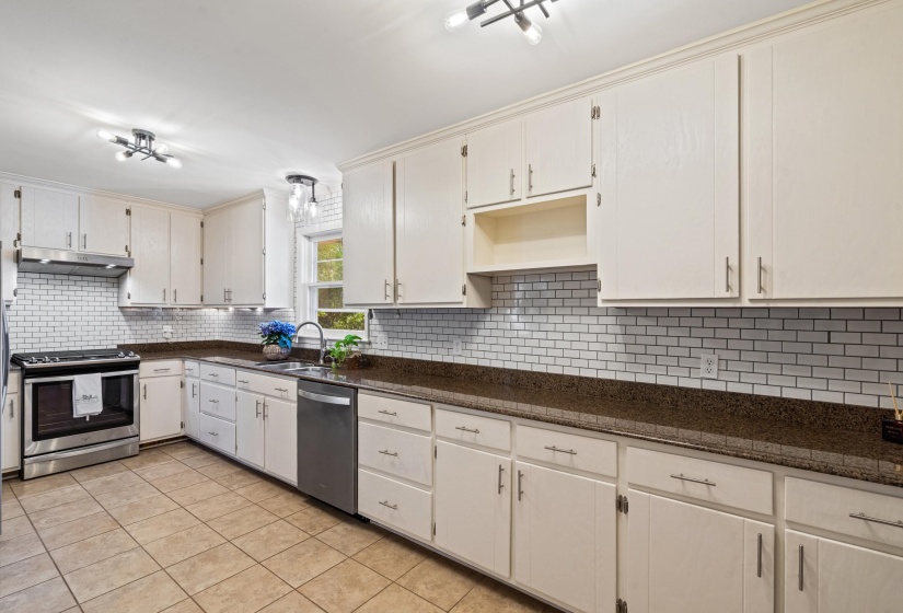 Kitchen featuring extensive white cabinetry, dark countertops, a subway tile backsplash, stainless steel appliances, and tiled flooring