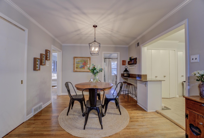 Dining area featuring wood-finish flooring, a contemporary pendant light fixture, and crown molding