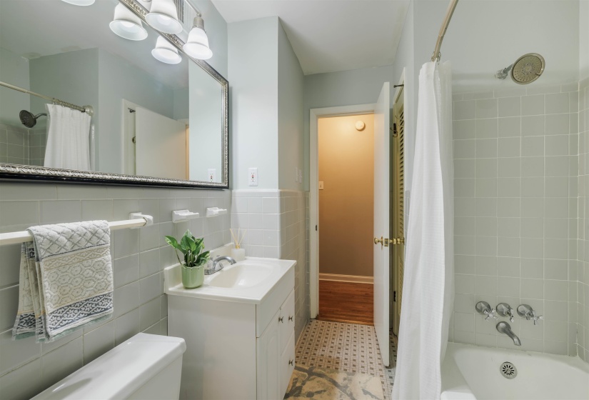 Full bathroom featuring a white vanity with integrated sink, silver-framed mirror, and a three-bulb light fixture