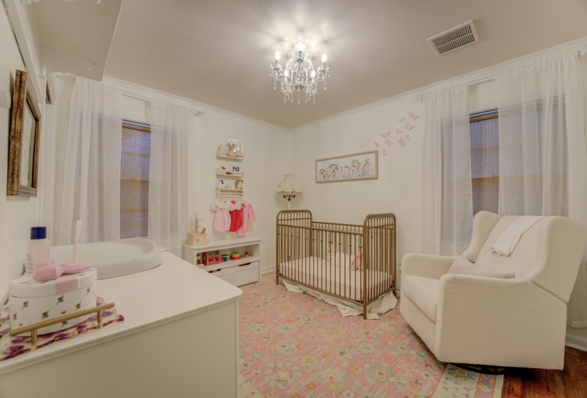 Bright room featuring a crystal chandelier, crown molding, two windows with sheer curtains, a white built-in wall shelf, and wood-finish flooring
