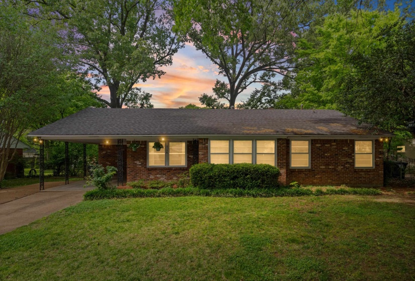 Brick single-story residence featuring a carport with decorative iron supports, a paved driveway, and established landscaping
