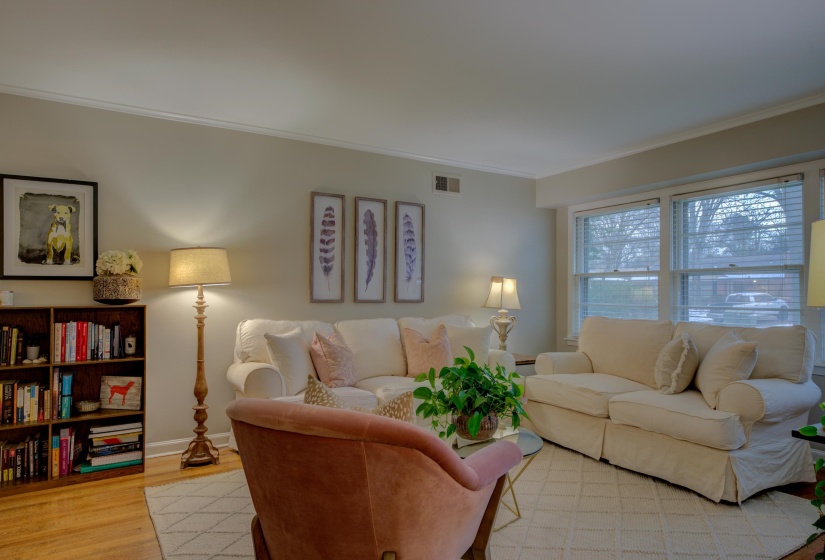 Bright interior space featuring wood-finish flooring, a large window, crown molding, and neutral wall tones