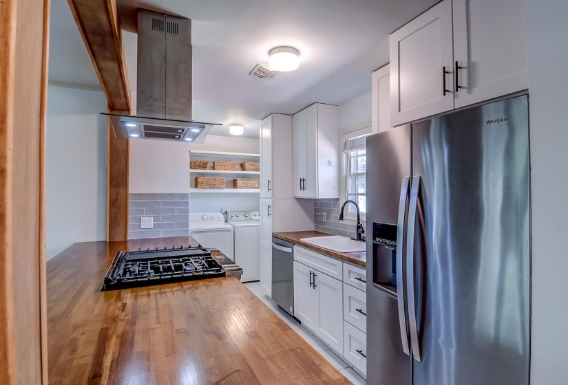Kitchen with stainless steel appliances, wooden counters, island range hood, white cabinetry, and washing machine and dryer