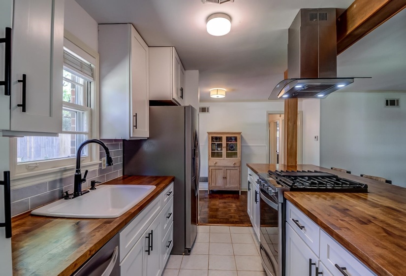 Kitchen with butcher block countertops, stainless steel appliances, island exhaust hood, and white cabinets