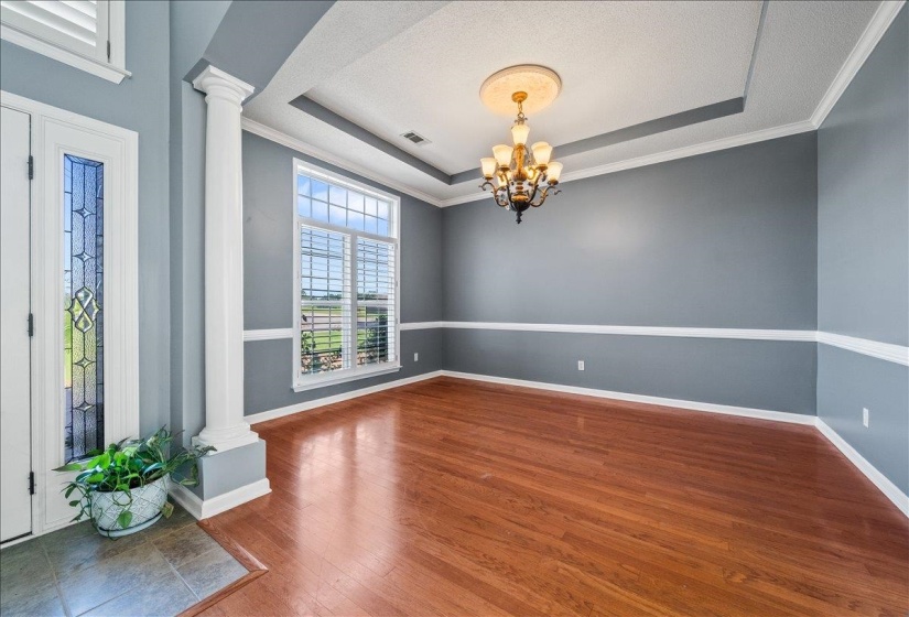 Empty room featuring ornate columns, a raised ceiling, a chandelier, dark wood-style flooring, and ornamental molding